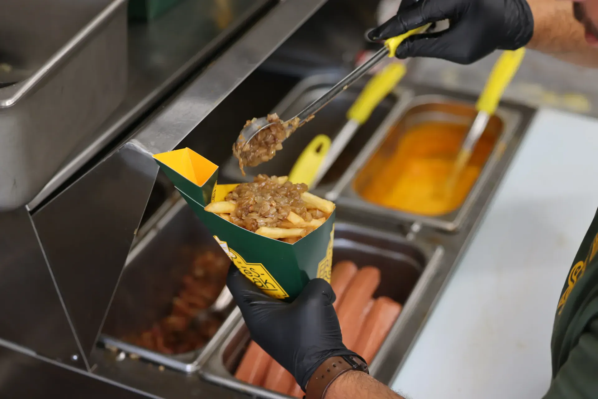 Grilled onions being spooned over a box of FRitēS-FReaK fries