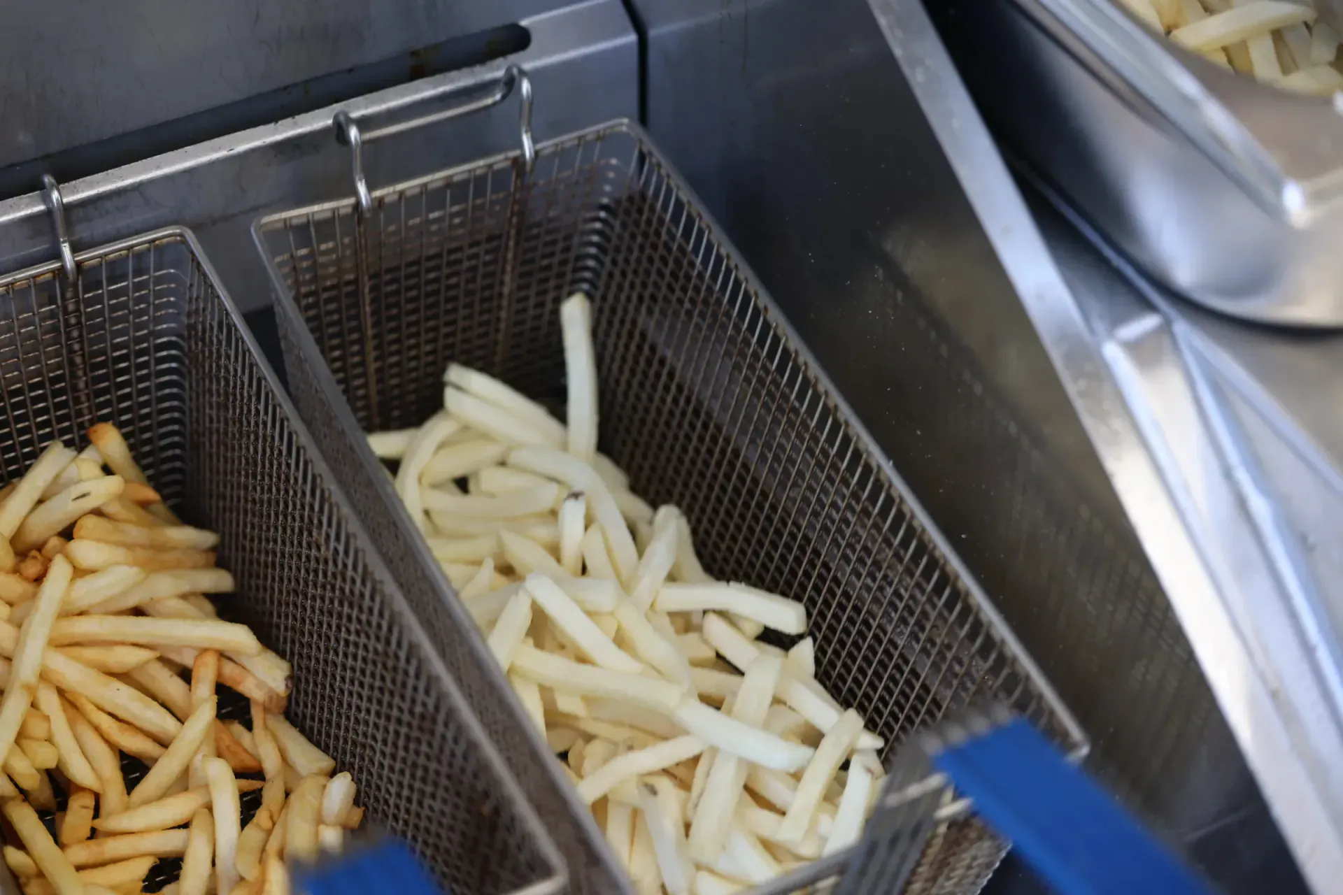 Two fryer baskets side by side — golden double-fried frites next to a fresh-cut batch