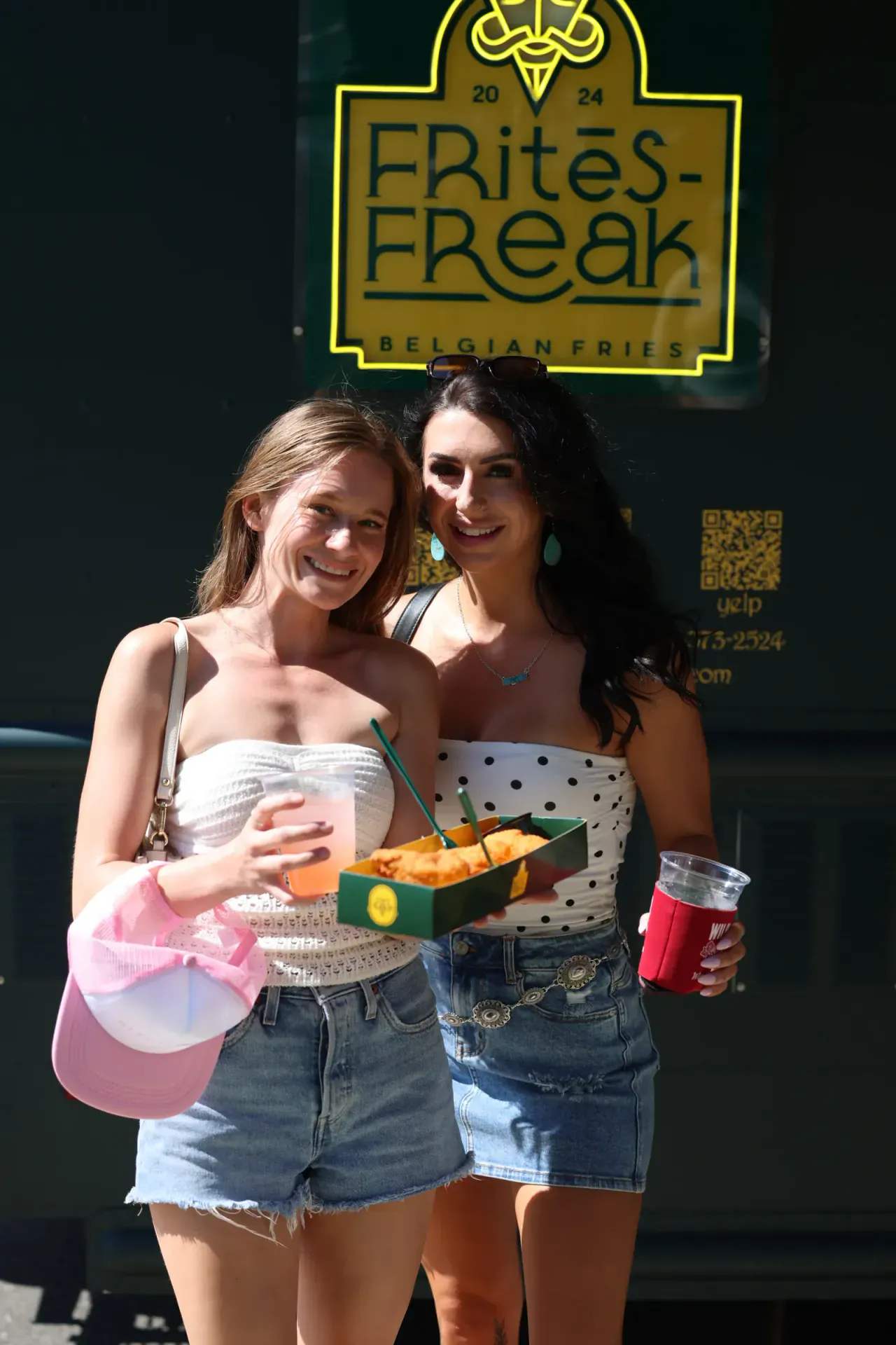 Two guests smiling with a tray of fries and drinks under the FRitēS-FReaK sign