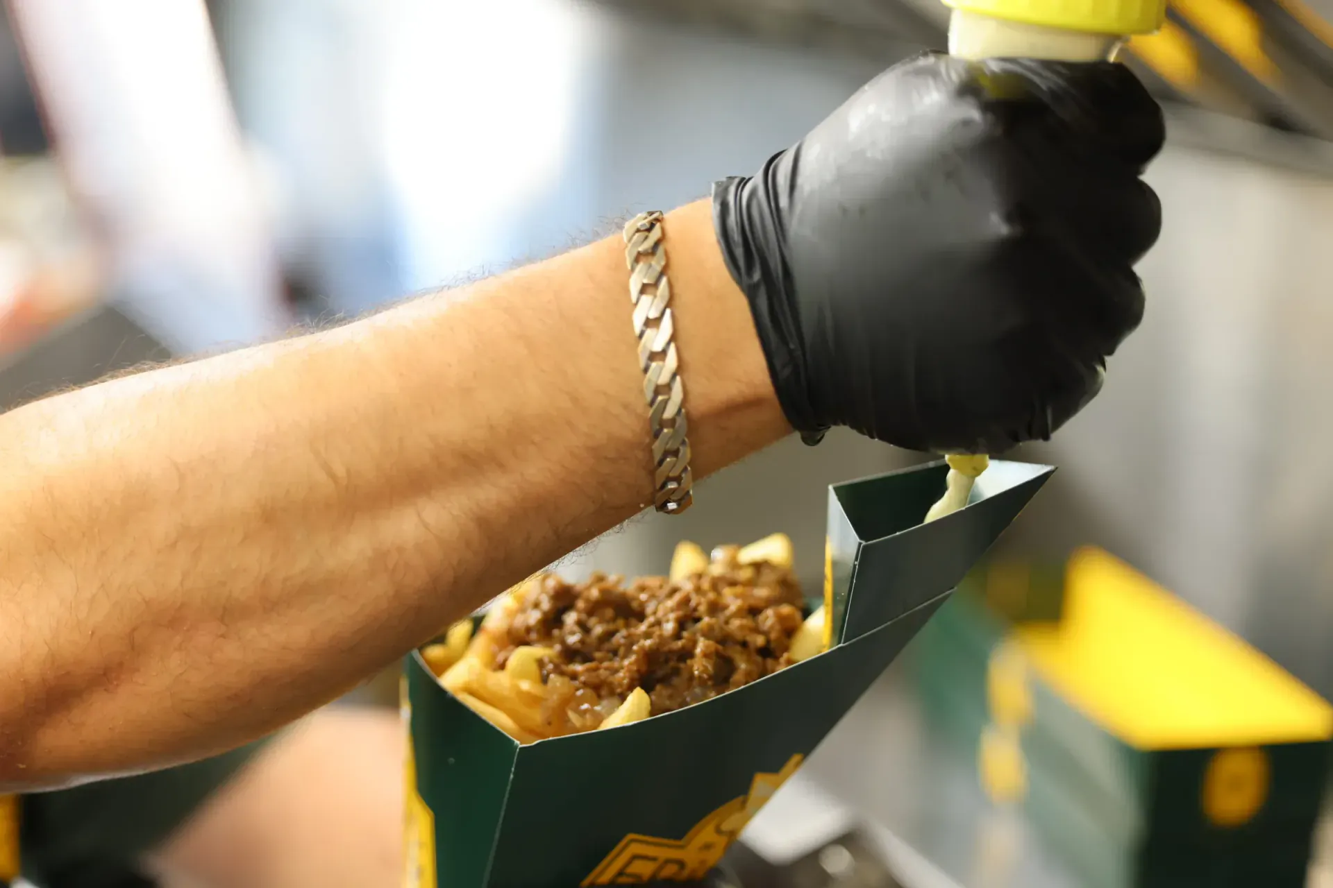 Sauce being squeezed over a box of beef-topped frites