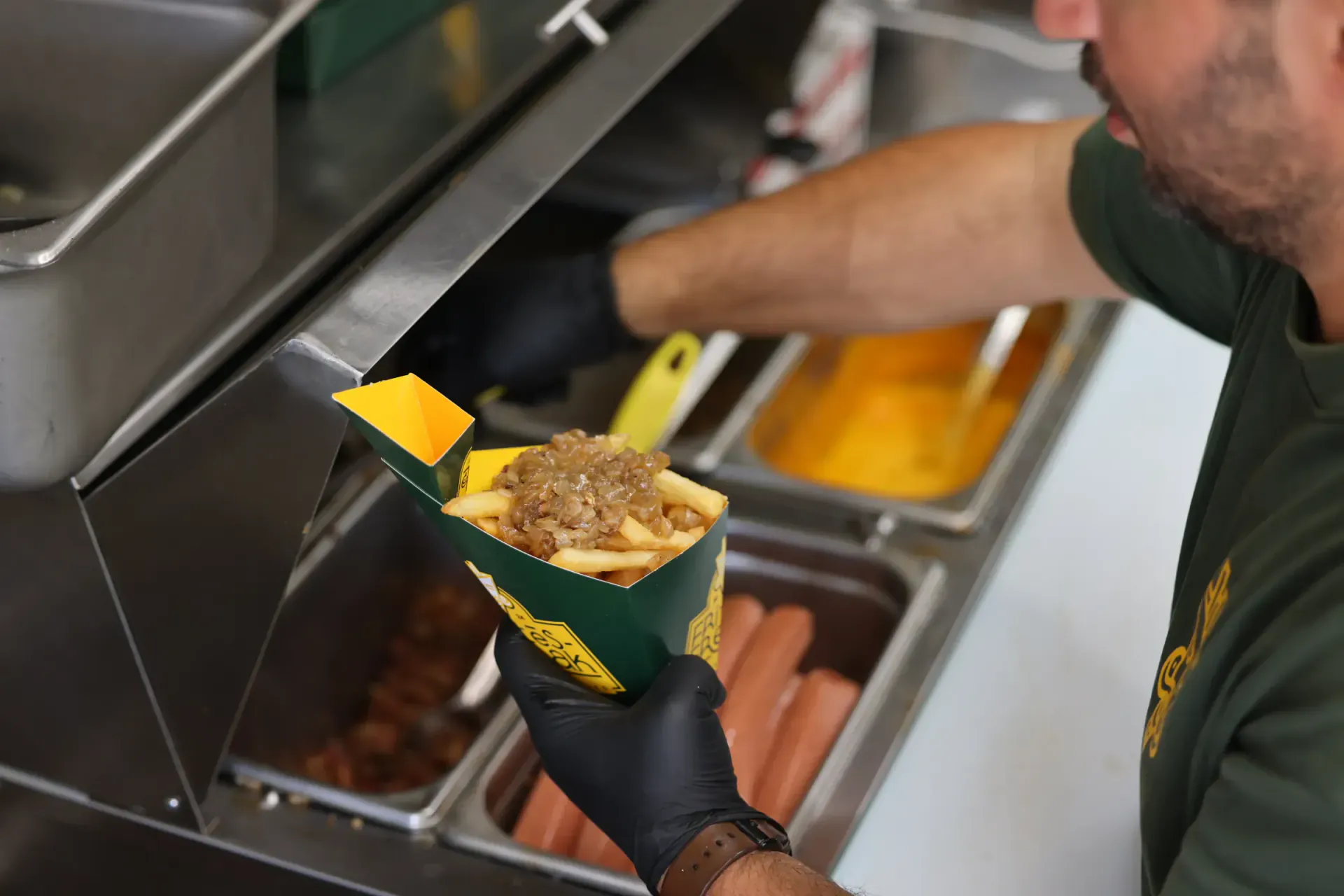 Toppings going onto a box of fries over the steam table